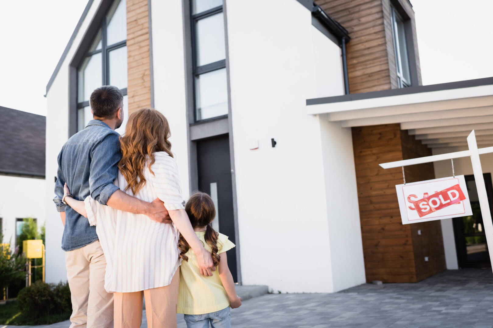 Back view of family near sign with sold lettering and house